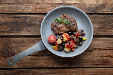 Photo of Tasty fried steak with vegetables in pan on wooden table, top view