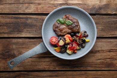 Tasty fried steak with vegetables in pan on wooden table, top view