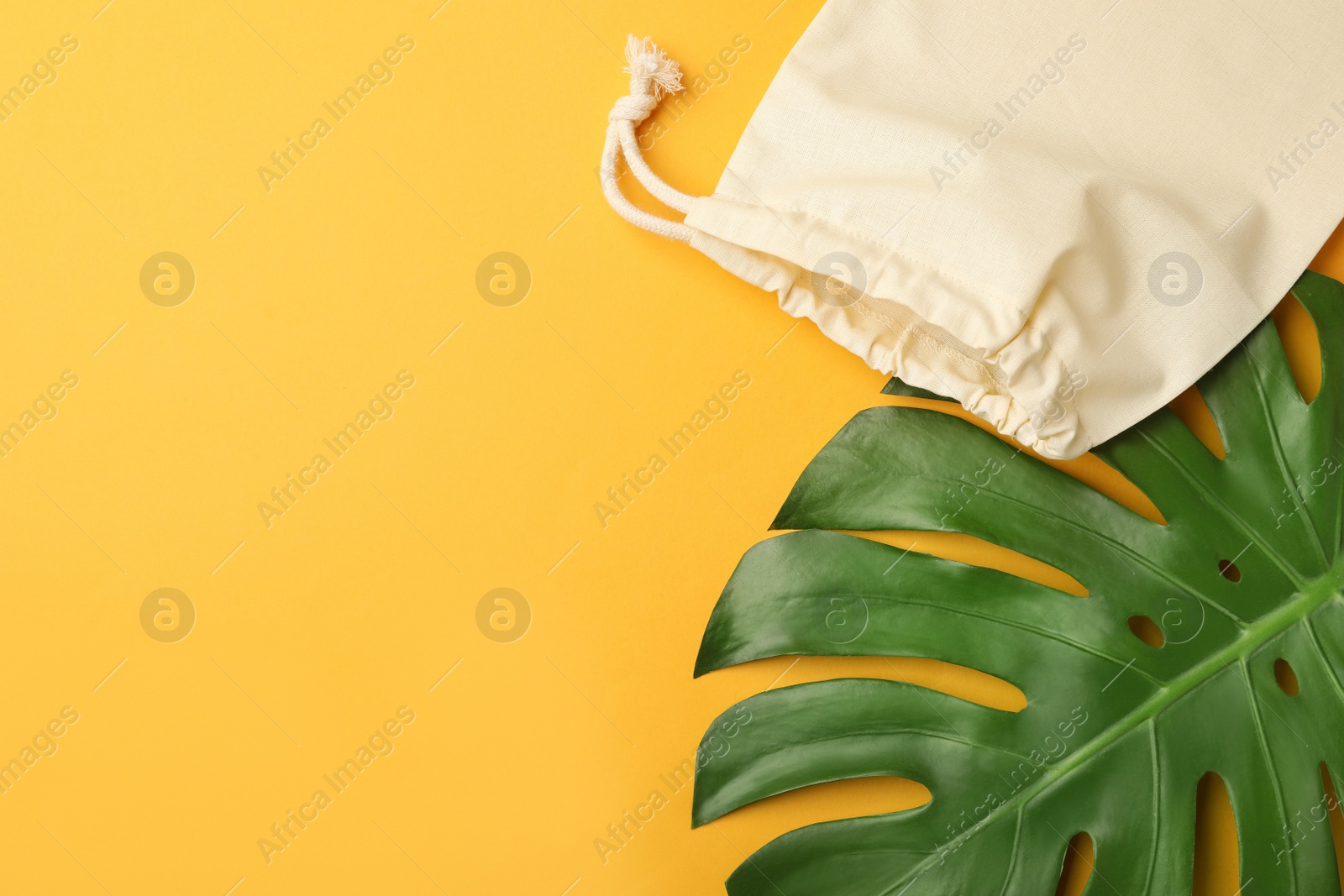 Photo of Cotton eco bag and leaf on yellow background, flat lay. Space for text