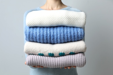 Woman holding pile of winter sweaters on grey background, closeup view