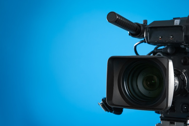 Photo of Professional video camera on blue background, closeup. Space for text