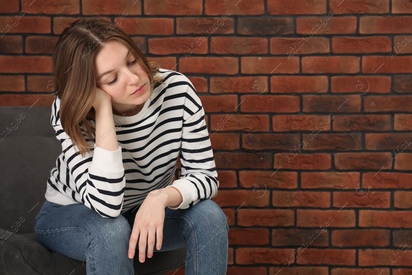 Photo of Sad young woman sitting on chair near brick wall, space for text