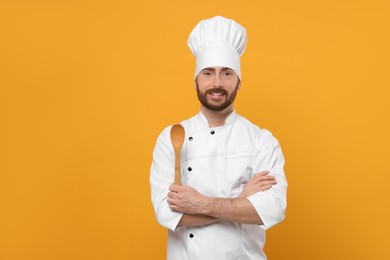 Photo of Smiling mature chef with spoon on orange background, space for text