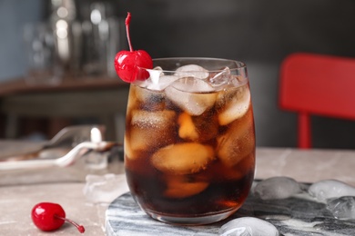 Photo of Tasty cola with ice cubes and cherry on table indoors