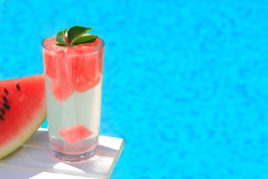 Photo of Refreshing watermelon drink in glass near swimming pool outdoors. Space for text