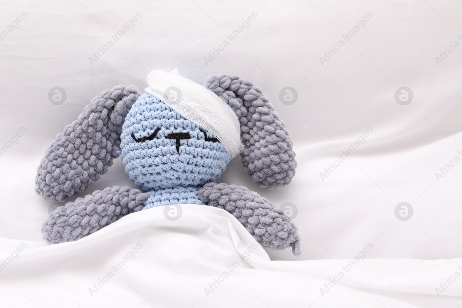 Photo of Toy cute bunny with bandage under blanket in bed