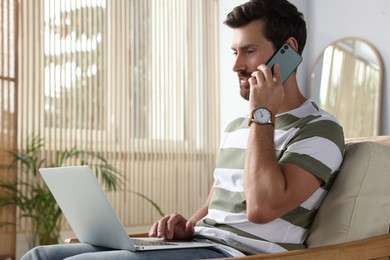 Handsome man talking on smartphone while working with laptop at home