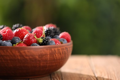 Bowl with different fresh ripe berries on wooden table outdoors, closeup. Space for text