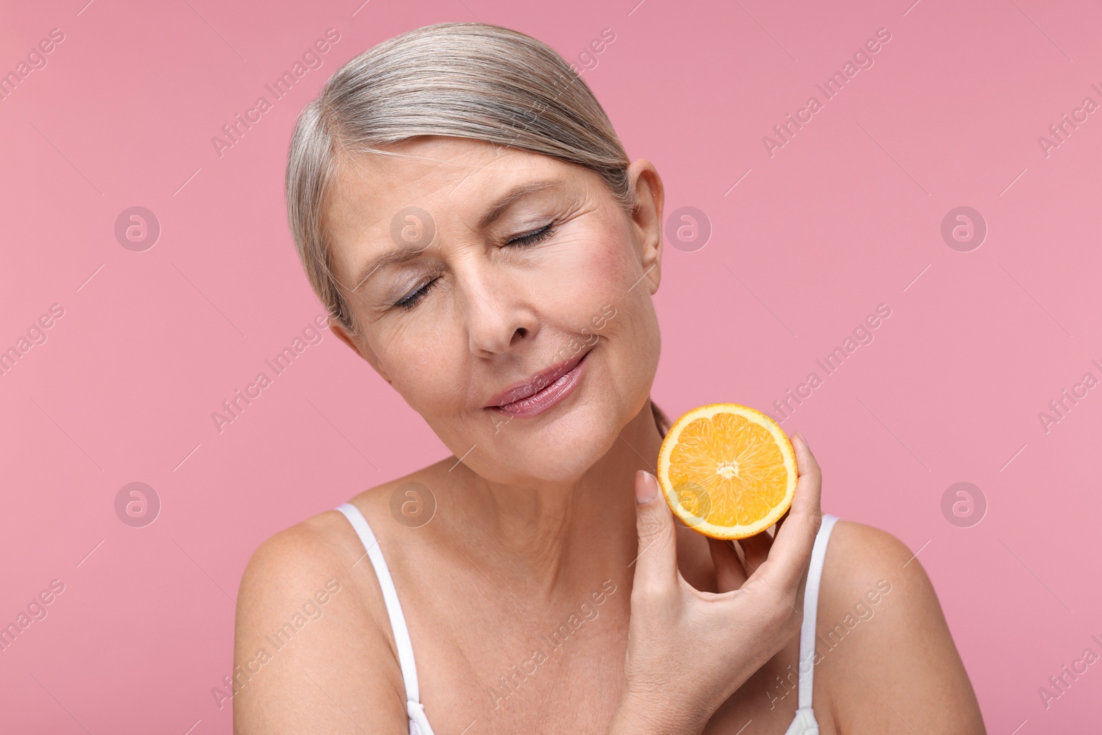 Photo of Beautiful woman with half of orange rich in vitamin C on pink background