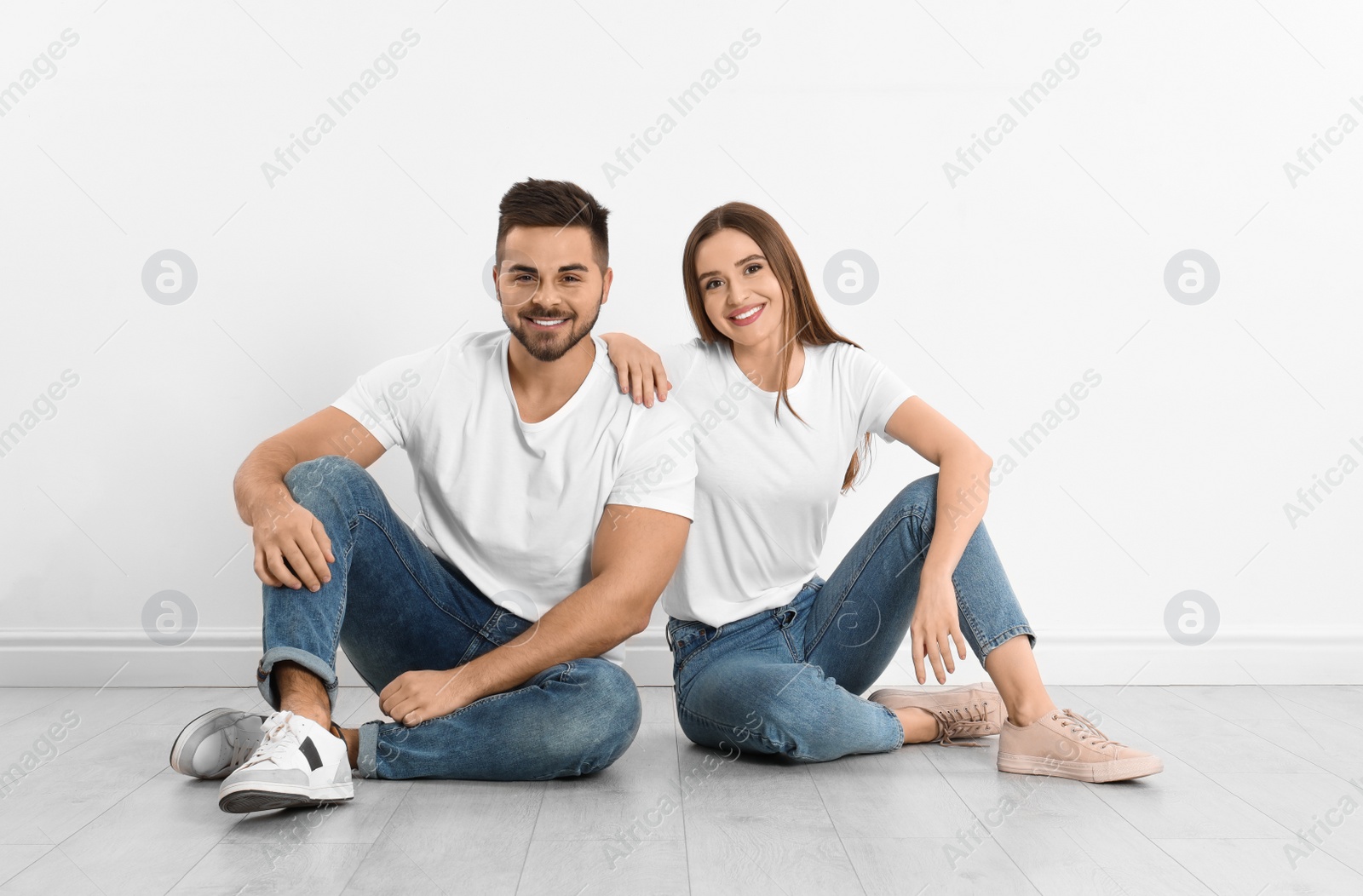 Photo of Young couple in stylish jeans sitting near white wall