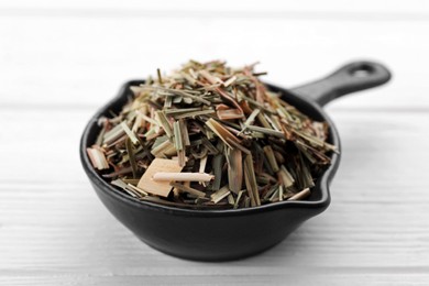 Photo of Small saucepan with aromatic dried lemongrass on white wooden table, closeup