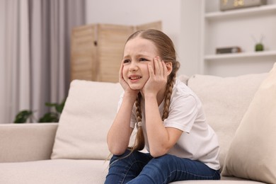 Little girl suffering from headache on sofa indoors