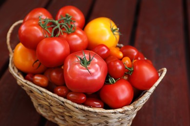 Photo of Wicker basket with fresh tomatoes on wooden table, closeup