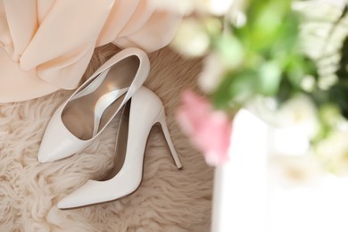 Photo of Pair of white high heel shoes and wedding dress on fuzzy rug, top view