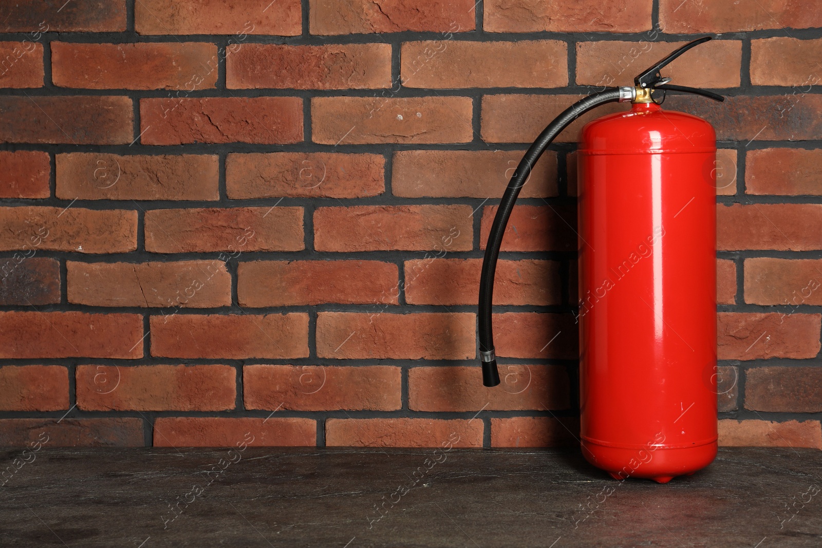 Photo of One red fire extinguisher near brick wall, space for text