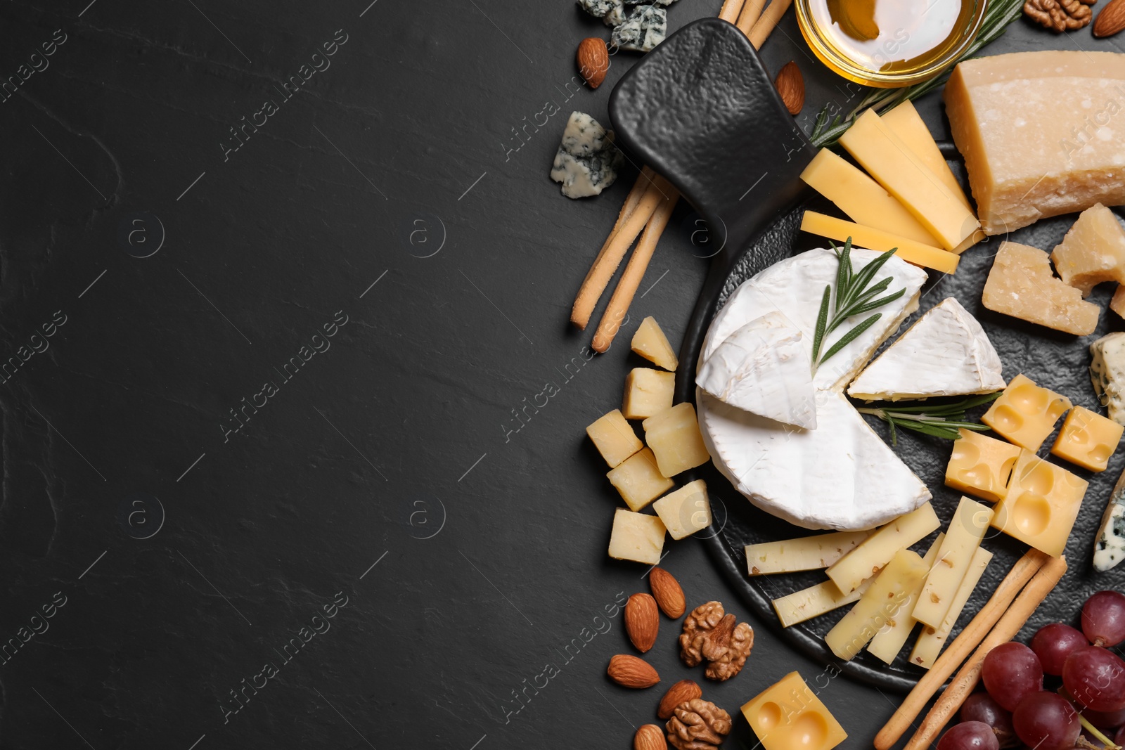 Photo of Cheese plate with honey, grapes and nuts on black table, flat lay. Space for text