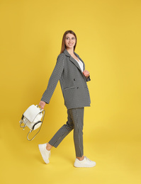 Beautiful young woman with stylish bag on yellow background