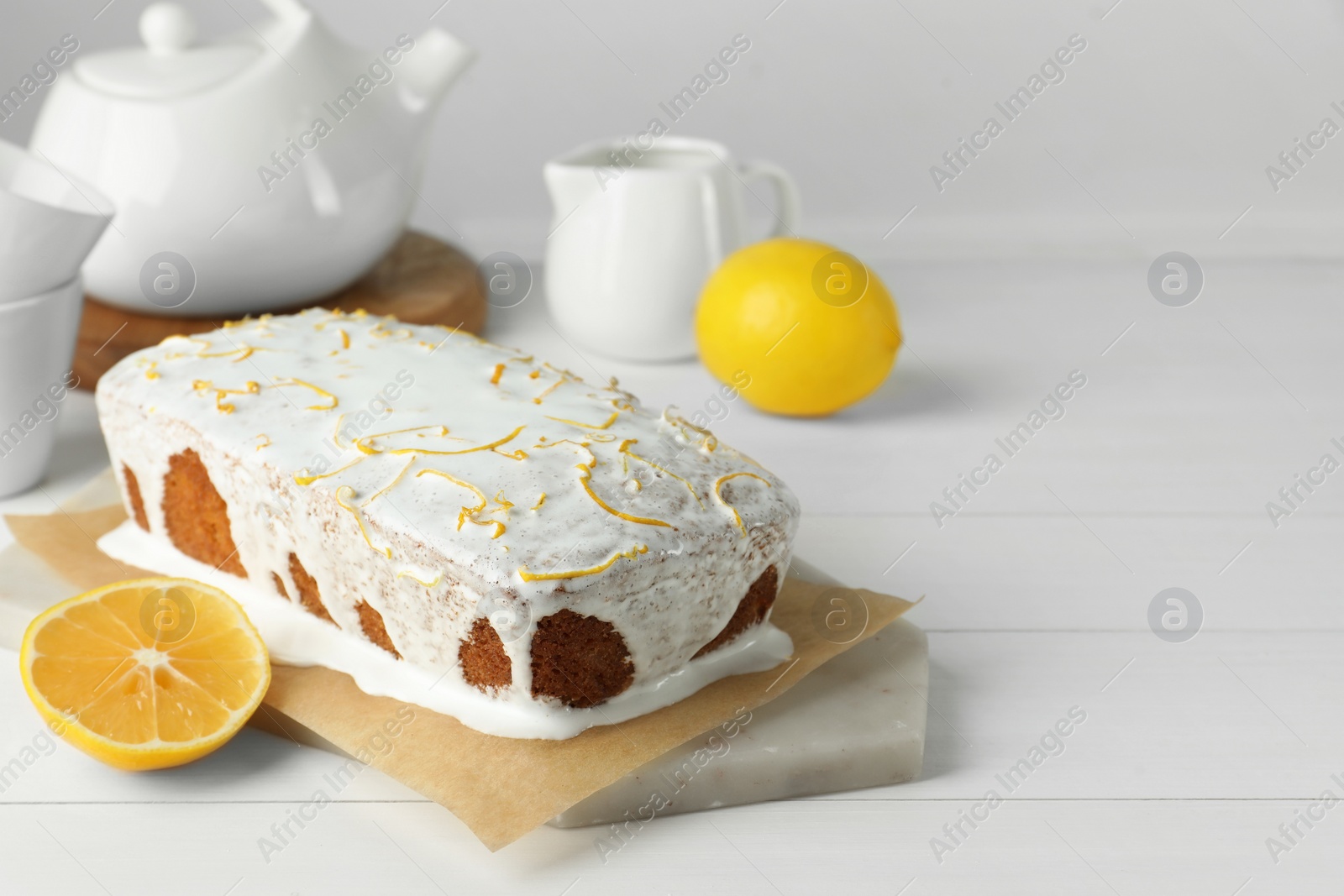 Photo of Tasty lemon cake with glaze and citrus fruits on white wooden table. Space for text