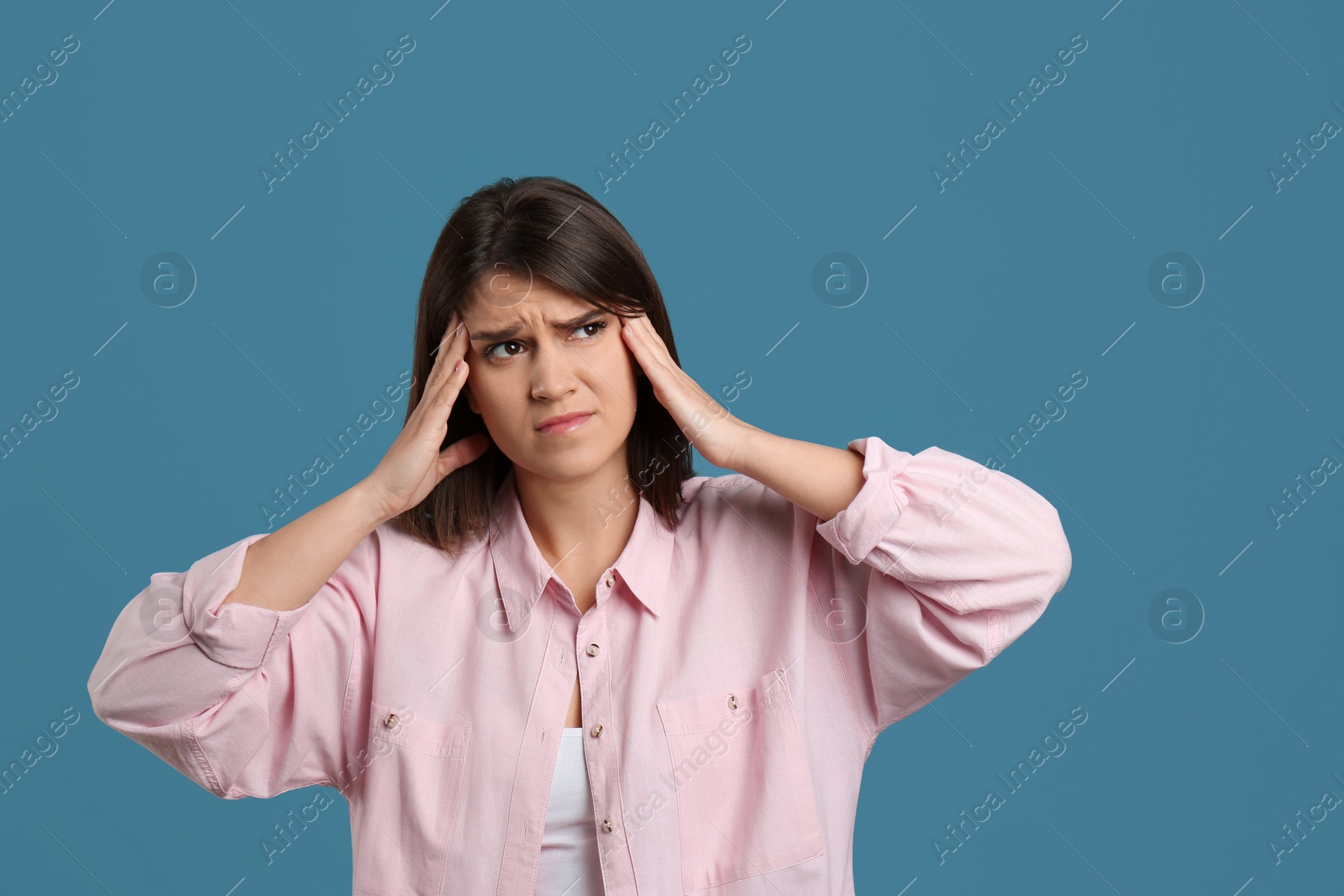 Photo of Young woman suffering from migraine on light blue background