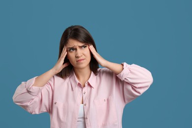 Young woman suffering from migraine on light blue background