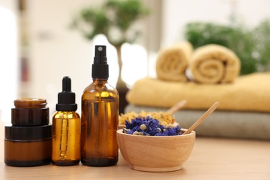 Bottles of essential oils, dry flowers and jars with cream on light wooden table, closeup. Spa therapy