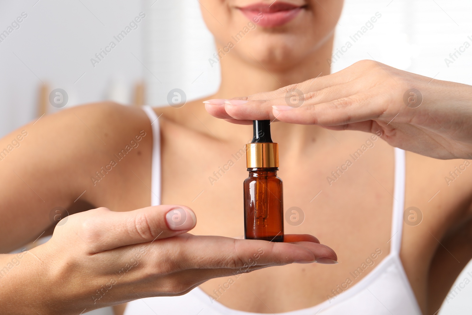 Photo of Woman with bottle of cosmetic serum on light background, closeup