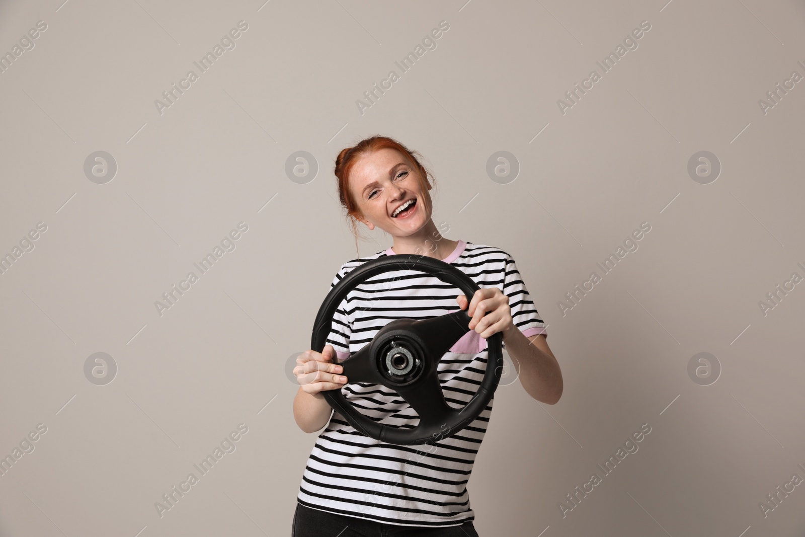 Photo of Happy young woman with steering wheel on grey background