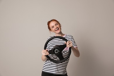 Happy young woman with steering wheel on grey background