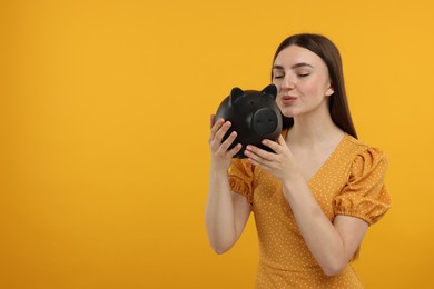 Woman with piggy bank on orange background, space for text