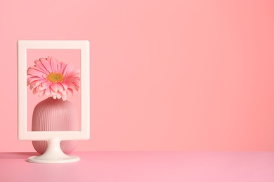 Photo of Vase with flower and photo frame on table against color background, space for text. International Women's Day