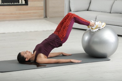 Photo of Young woman doing exercise with fitness ball at home