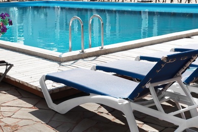 Photo of Comfortable loungers at clean swimming pool on sunny day