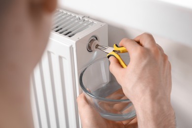 Photo of Professional repairman fixing heating radiator with pliers indoors, closeup