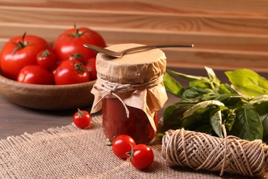 Jar of tasty tomato paste with spoon, ingredients and thread on wooden table