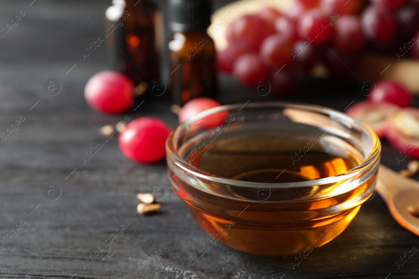 Photo of Glass bowl with natural grape seed oil on black wooden table, space for text. Organic cosmetic