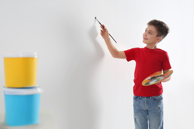 Photo of Little child painting on blank white wall indoors, space for text