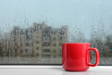 Cup of hot drink on windowsill, space for text. Rainy weather