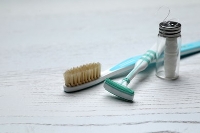 Photo of Tongue cleaner, toothbrush and dental floss on white wooden table, closeup. Space for text