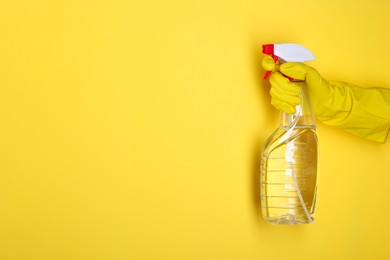 Photo of Woman holding plastic spray bottle on yellow background, closeup. Space for text