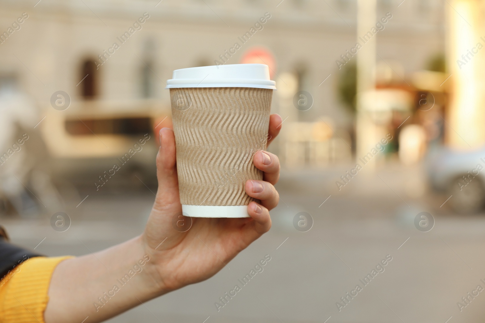 Photo of Woman holding paper takeaway cup on city street, closeup with space for text. Coffee to go