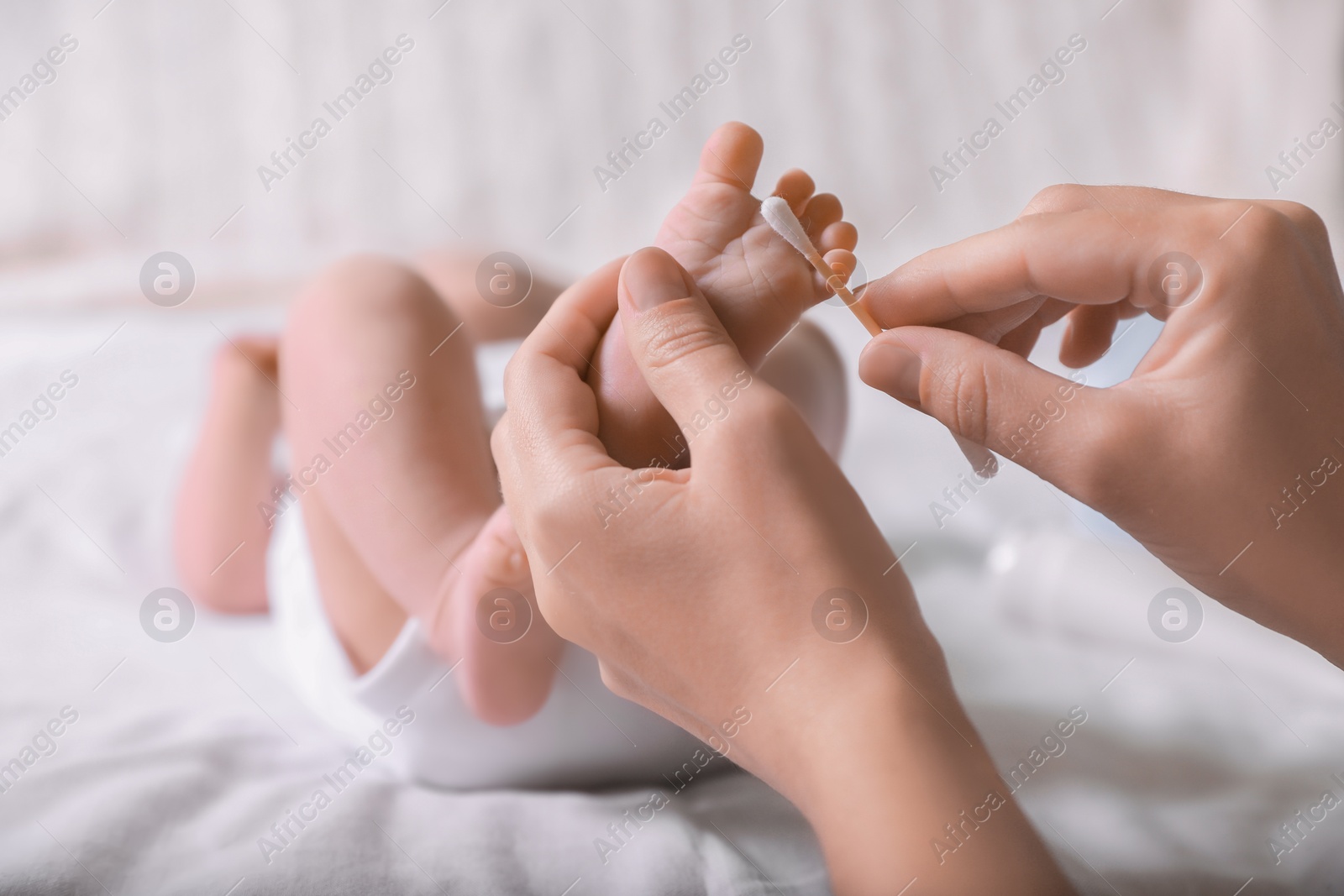 Photo of Mother cleaning baby's foot with cotton bud on bed, closeup