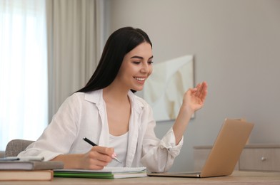 Young woman taking notes during online webinar at table indoors
