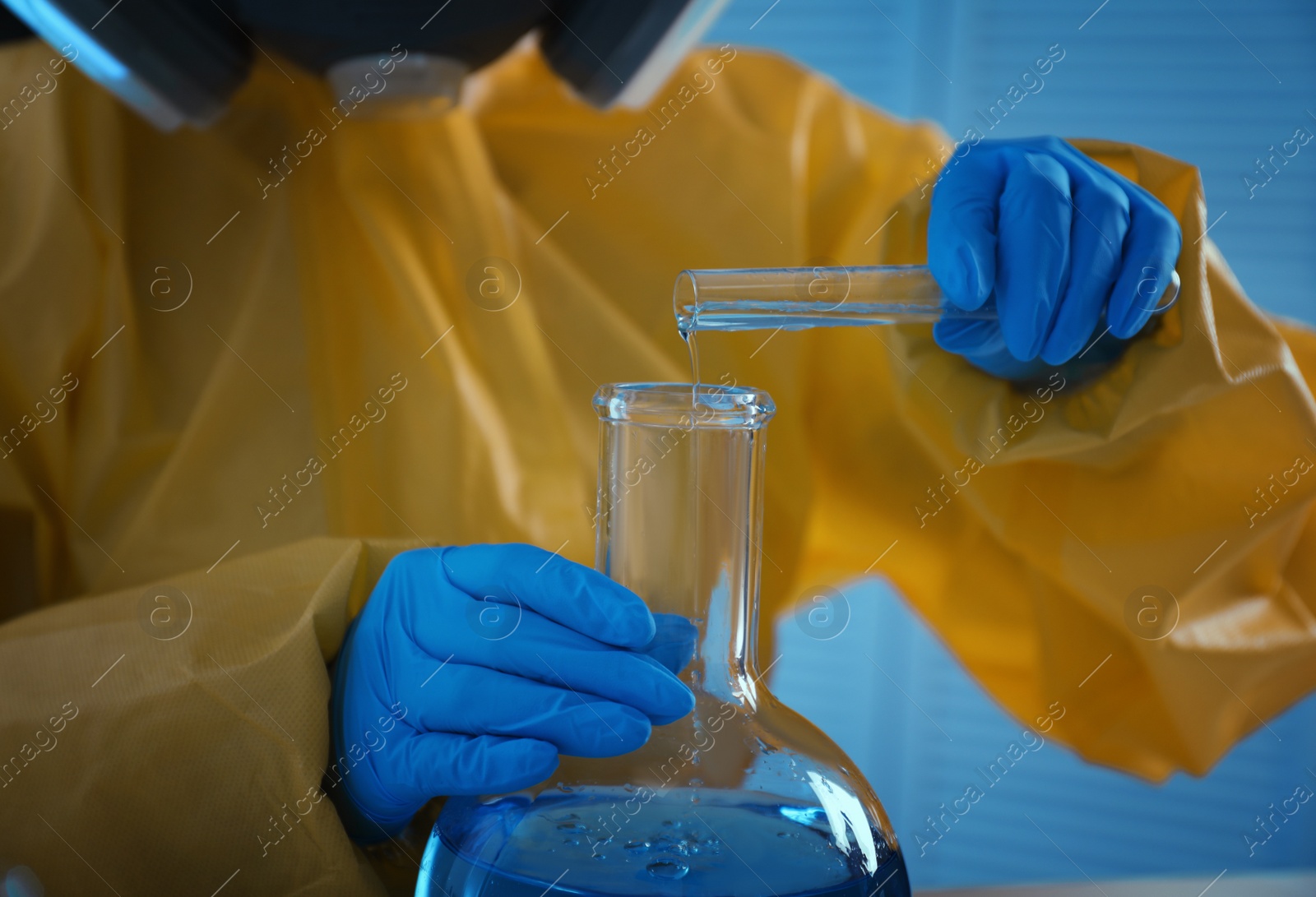 Photo of Scientist in chemical protective suit pouring reagent into flask at laboratory, closeup. Virus research