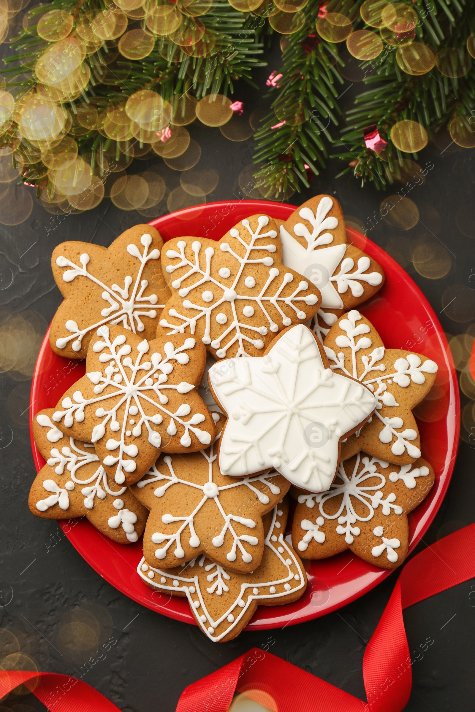Photo of Tasty Christmas cookies with icing, fir tree branches and ribbon on black table, flat lay