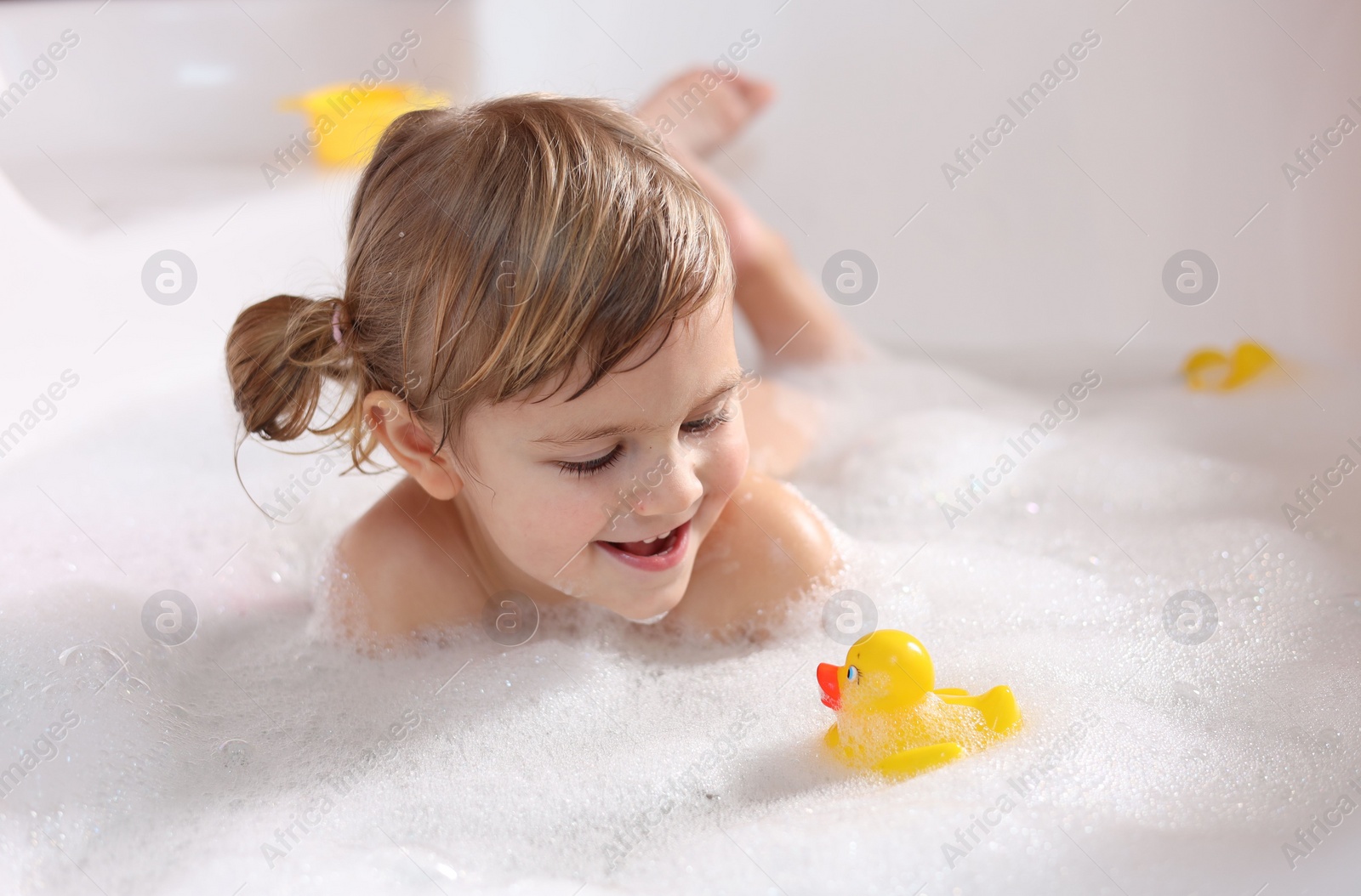 Photo of Smiling girl bathing with toy duck in tub