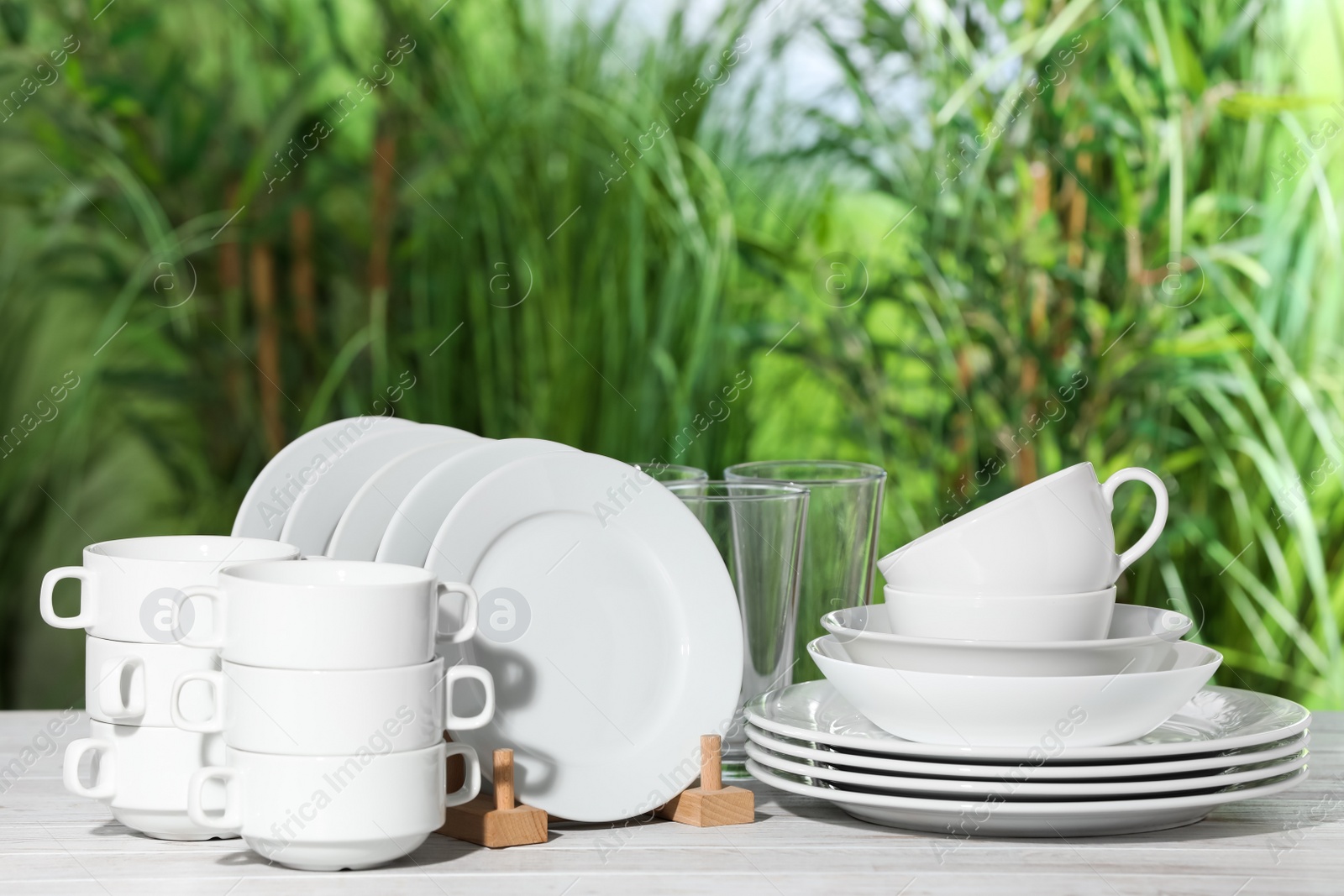 Photo of Set of clean dishware on white table against blurred background