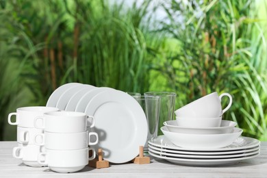 Set of clean dishware on white table against blurred background