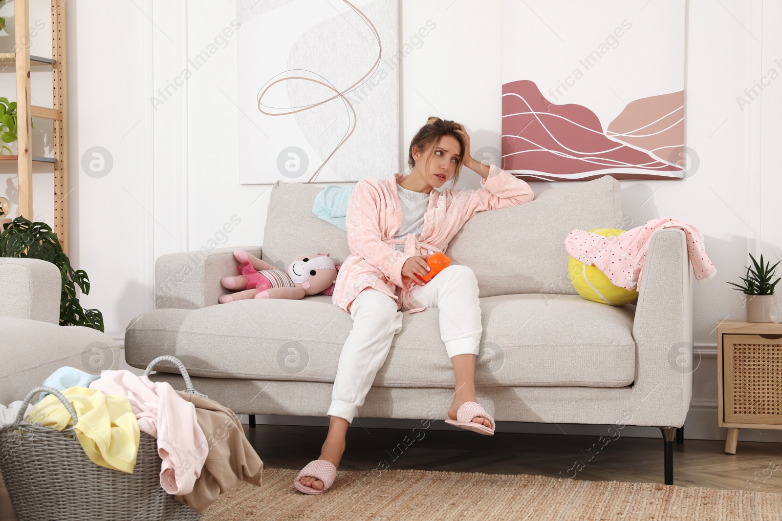 Photo of Tired young mother sitting on sofa in messy living room