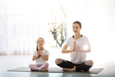 Young mother with little daughter practicing yoga at home