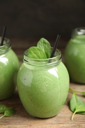 Photo of Jars of healthy green smoothie with fresh spinach on wooden table